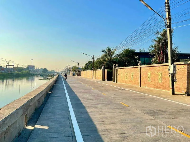 Detached House for sale in Khlong Luang, Pathum Thani - Canal-side concrete road running along the property’s long brick boundary wall.