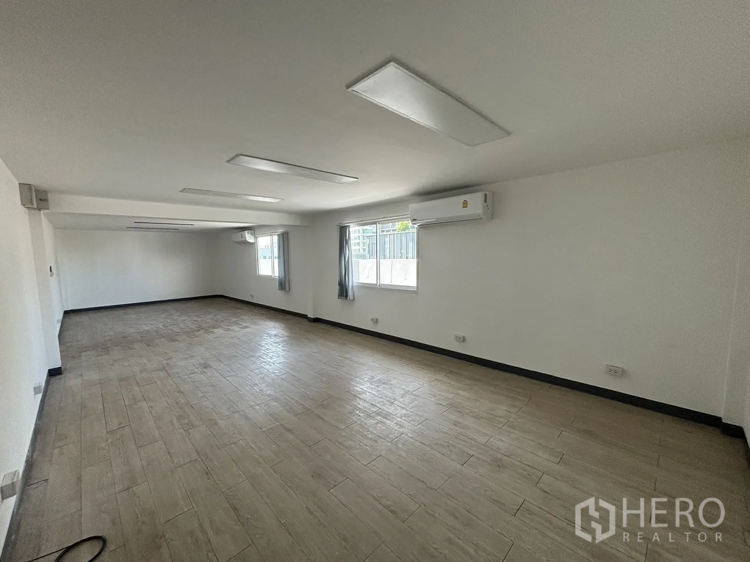 Office Space for rent in Watthana, Bangkok - Large open-plan office with windows, wall air conditioners and tile flooring.