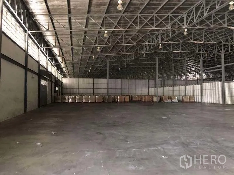 Warehouse for rent in Bang Phli, Samut Prakan - Large warehouse space with pallets along the wall and steel roof trusses.