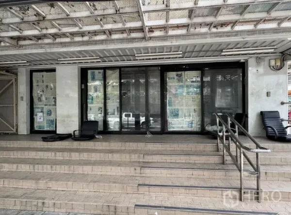 店屋 出租在Watthana, Bangkok - 临街商铺门面，金属雨棚下设台阶、无障碍坡道与玻璃移门。