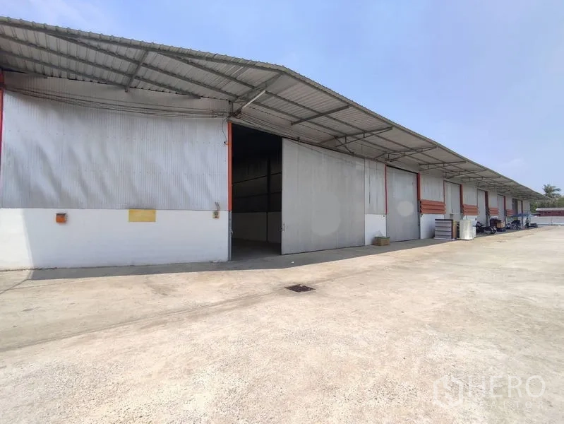 Warehouse for rent in Pathum Thani - Exterior of multiple warehouse bays with an open door and deep apron for loading and parking.