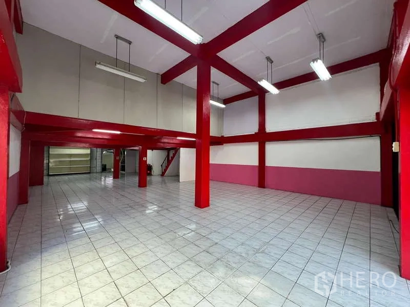 Shophouse for rent in Suan Luang, Bangkok - Double-height showroom with red steel columns, white tiled floor and hanging lights.