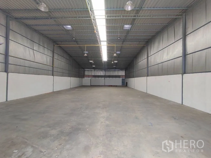 Warehouse for rent in Pathum Thani - Wide open storage hall showing high ceiling, insulated metal walls and central skylight lighting.