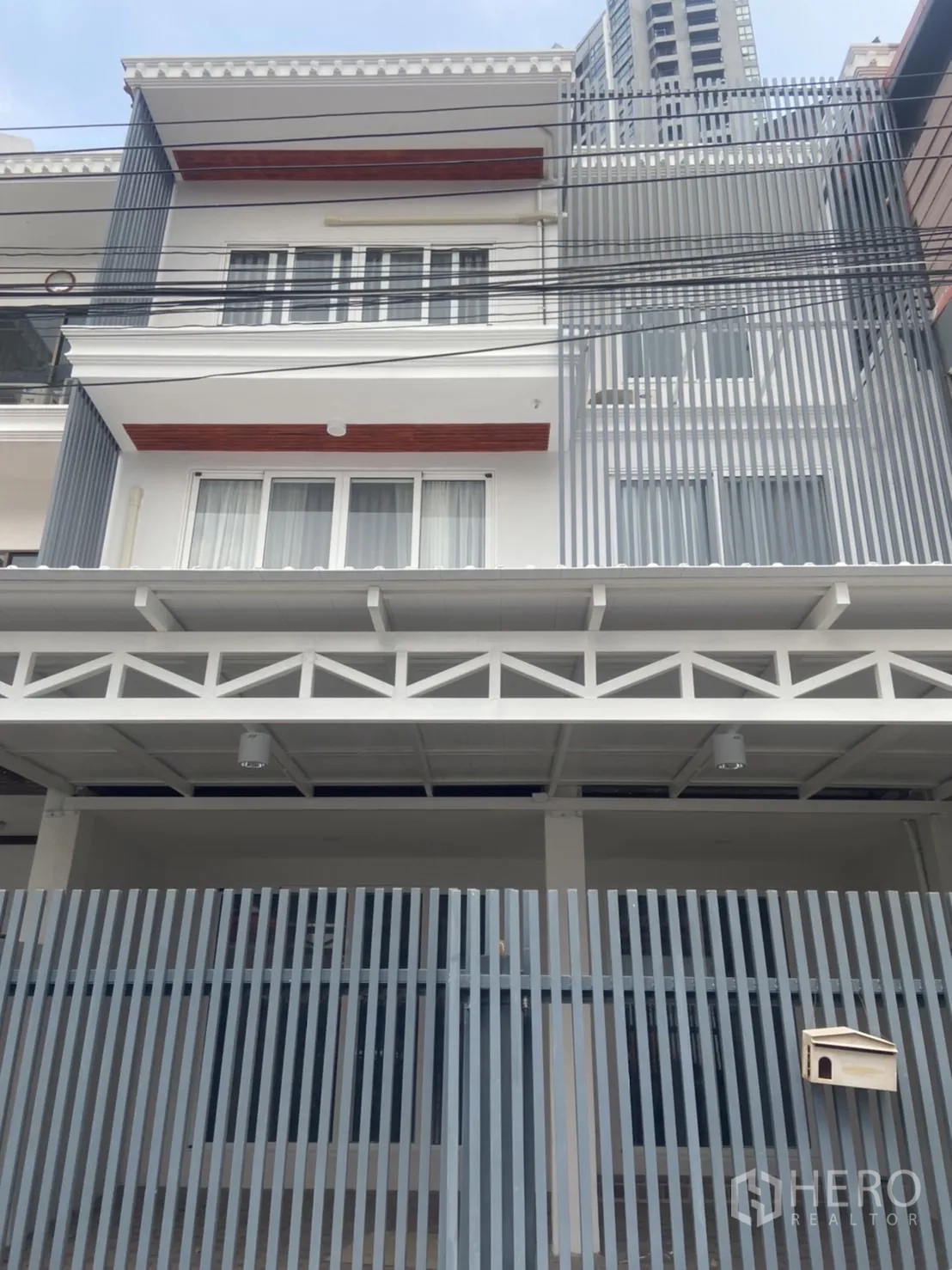 Townhouse for rent in Khlong Toei, Bangkok - Modern multi-storey townhouse facade with vertical metal slats and a gated carport.