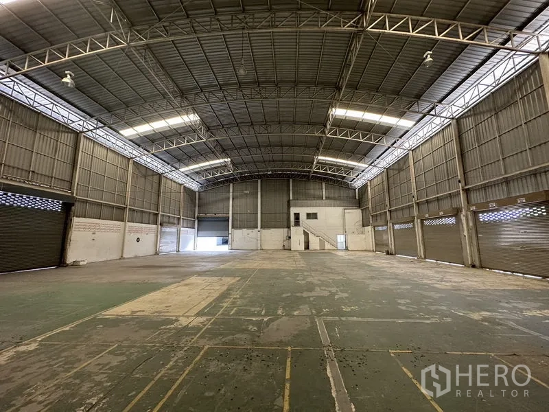 Factory for rent in Phra Nakhon Si Ayutthaya - Wide shot of open production floor under bright skylights with several roller shutters along one wall.