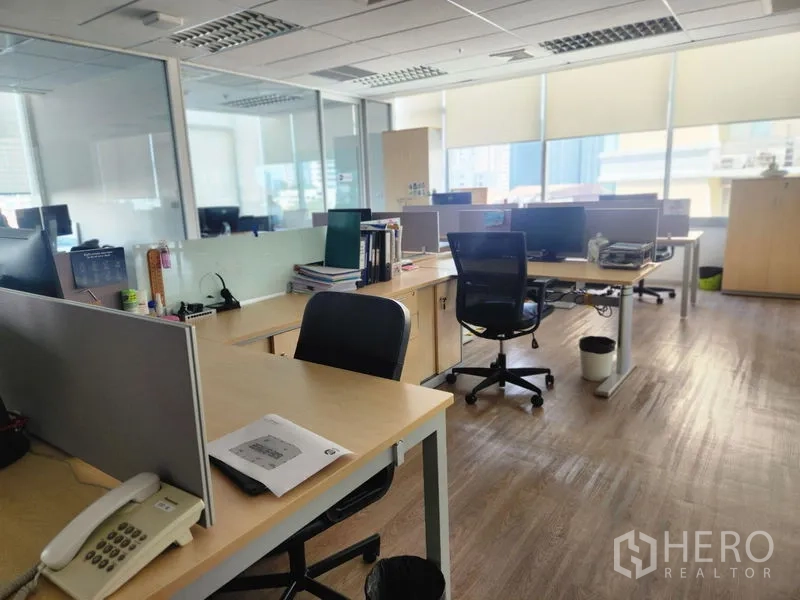 Office Space for rent - Clustered desks with phone and filing cabinets next to glass partitions and roller blinds.