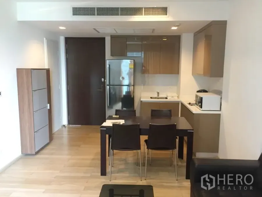 Condominium for rent in Khlong Toei, Bangkok - Open-plan kitchen and dining area with glossy cabinets, stainless refrigerator, and a four-seat table in a modern Bangkok condo.