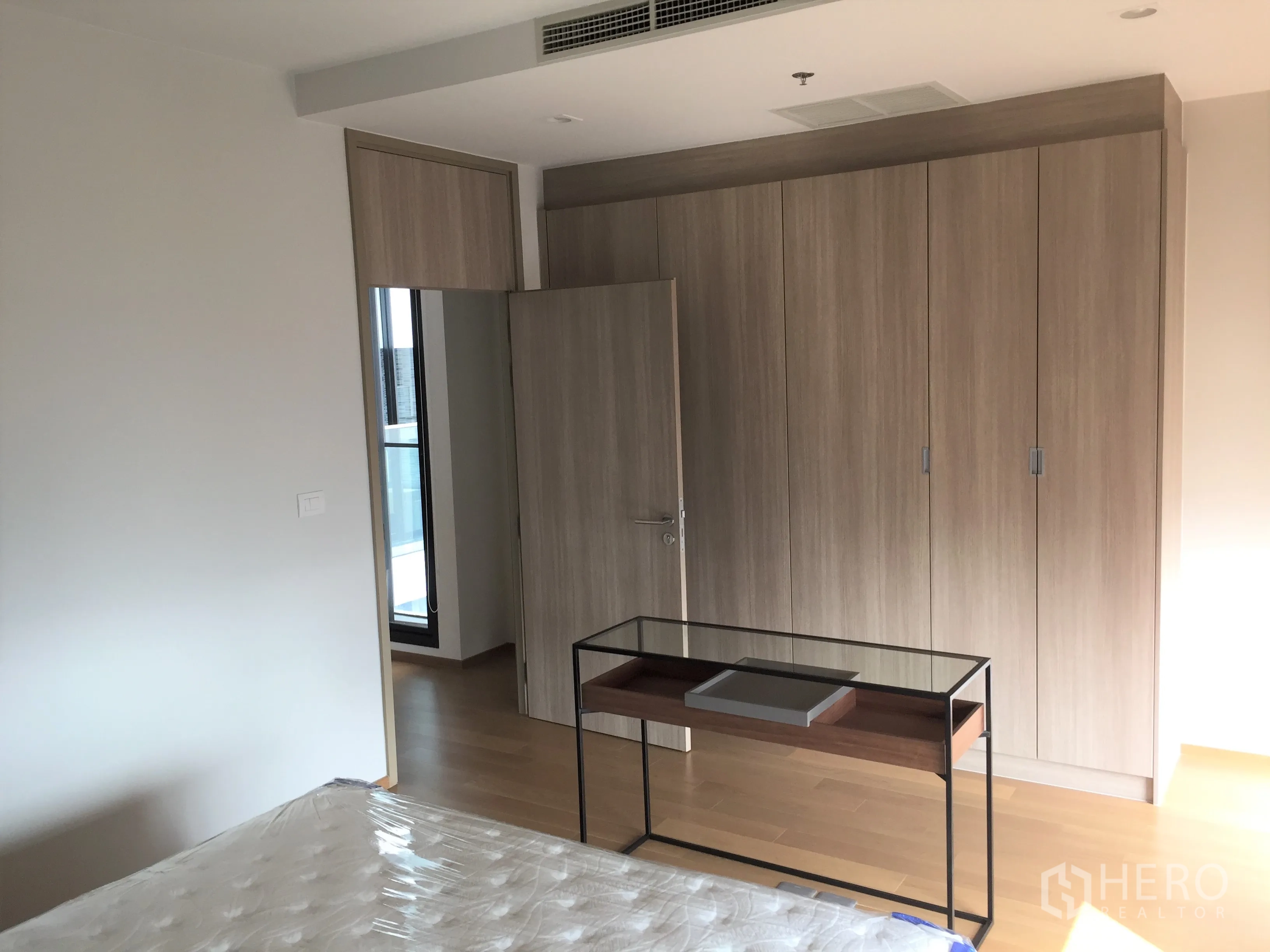 Condominium for rent in Pathum Wan, Bangkok - Bright bedroom featuring large built-in wardrobes and access to a balcony door.