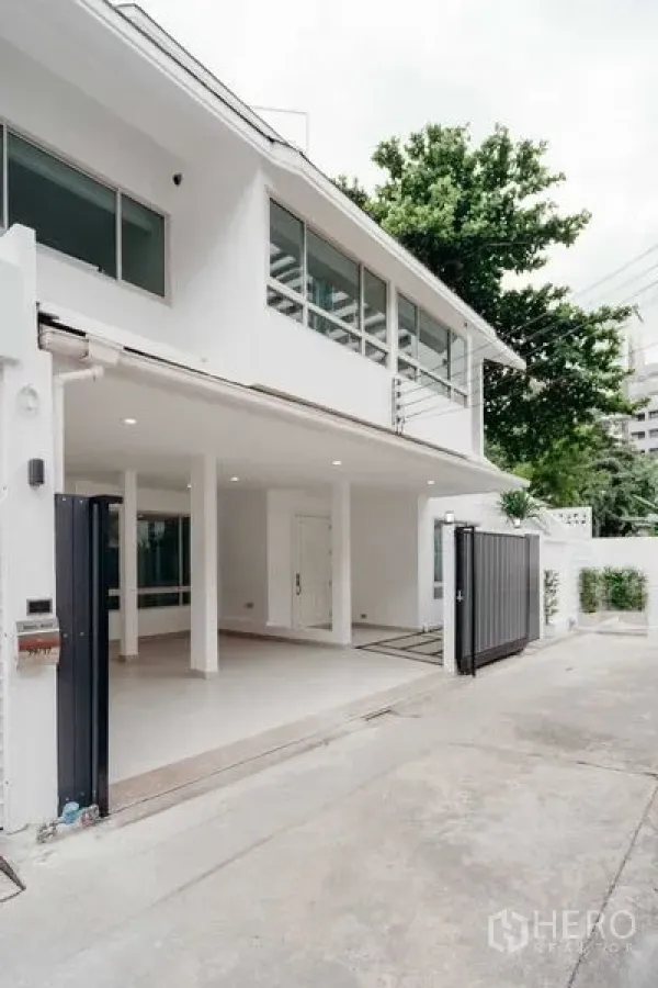 Detached House for sale in Watthana, Bangkok - Another view of the white two-storey facade with gated driveway and trees.