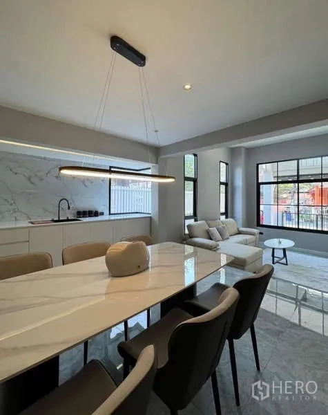 Townhouse for rent or sale in Prawet, Bangkok - Open-plan dining and lounge beside a marble-look kitchen wall.