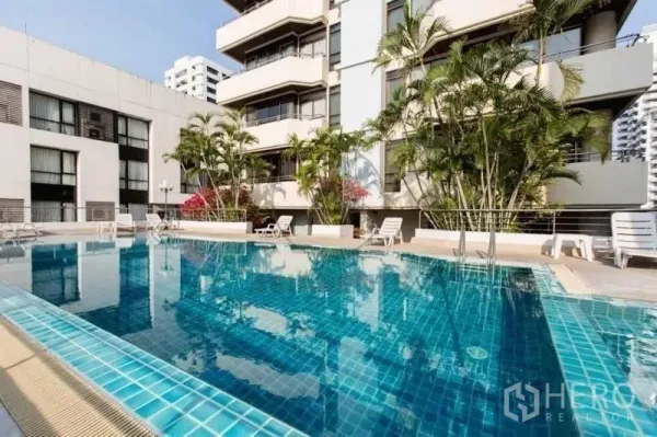 Condominium for rent in Khlong Toei, Bangkok - Outdoor swimming pool with sun loungers and tropical greenery beside the condo building.