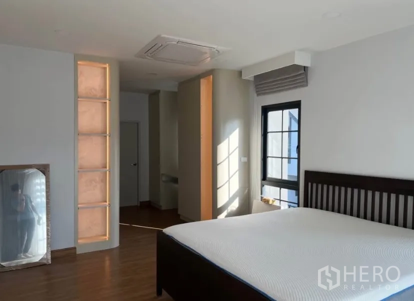 Detached House for rent in Bang Phli, Samut Prakan - Sunlit master bedroom with wooden floor, dark wood bed frame, window, ceiling cassette air-conditioner and illuminated wall niche.