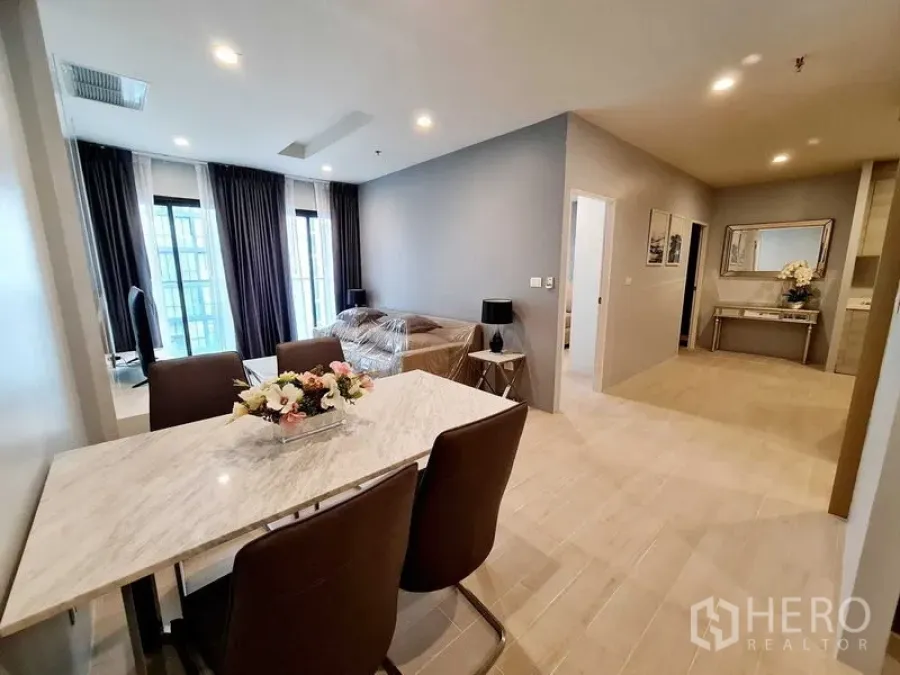 Condominium for rent in Pathum Wan, Bangkok - Open-plan dining and lounge with marble-top table, cushioned chairs, sofa, and tall windows.