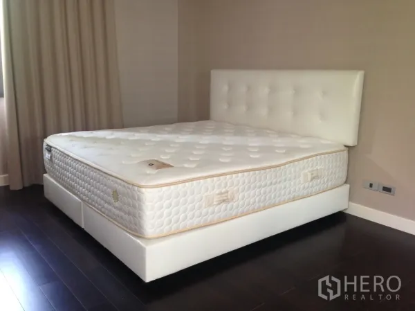 Townhouse for rent in Bang Kapi, Bangkok - Bedroom featuring a large white upholstered bed, dark wood flooring and neutral walls.
