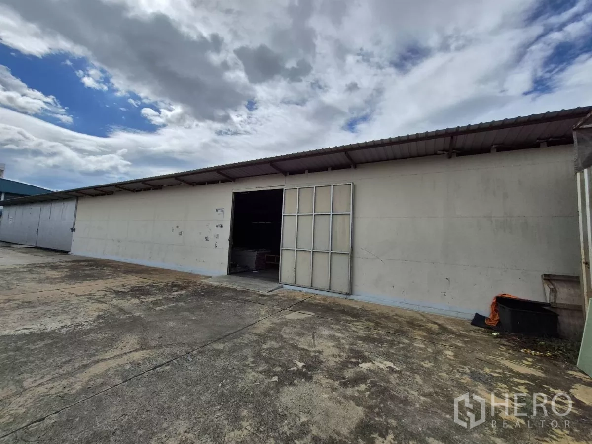 Warehouse for rent in Mueang Pathum Thani, Pathum Thani - Front view of ground-level warehouse facade with an open manual folding door and ample paved forecourt.