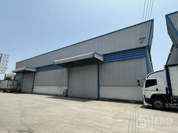 Warehouse for rent in Bang Phli, Samut Prakan - Side view of warehouse facade showing large roller doors, canopy loading areas and truck access.
