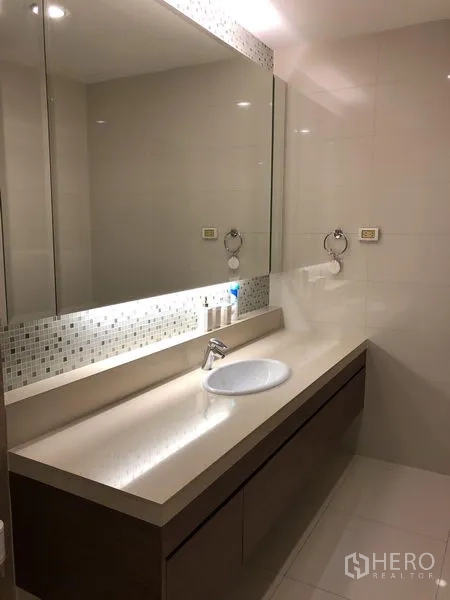 Condominium for rent or sale in Khlong Toei, Bangkok - Contemporary bathroom with long vanity, large mirror and soft lighting.