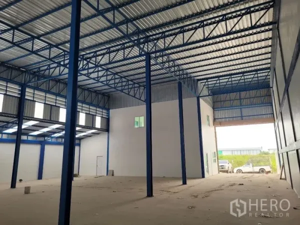 Factory for rent or sale in Khlong Luang, Pathum Thani - Warehouse bay with tall columns, internal office block, and wide roller door opening.