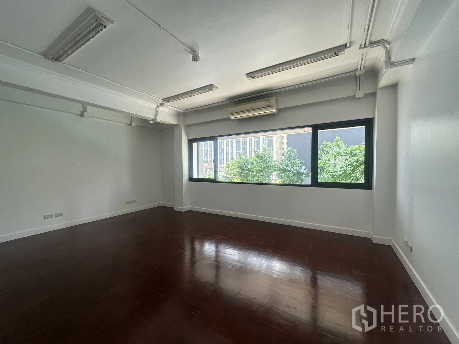 Office Space for rent in Watthana, Bangkok - Large office area with air conditioner and city and tree views through wide windows.
