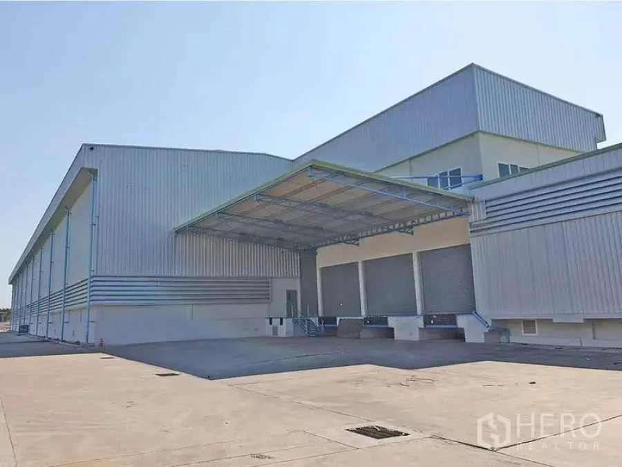 Warehouse for rent in Lat Krabang, Bangkok - Facade view showing multiple roller shutter loading docks under a canopy and ample yard space for truck maneuvering.