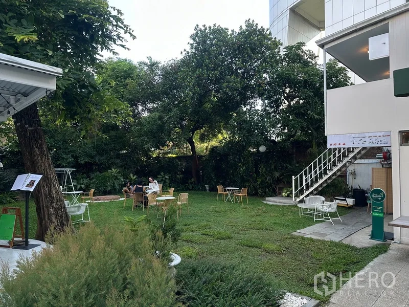 零售空间 for rent in Khlong Toei, Bangkok - 草坪庭院设有户外桌椅，旁边为楼梯与建筑一隅。
