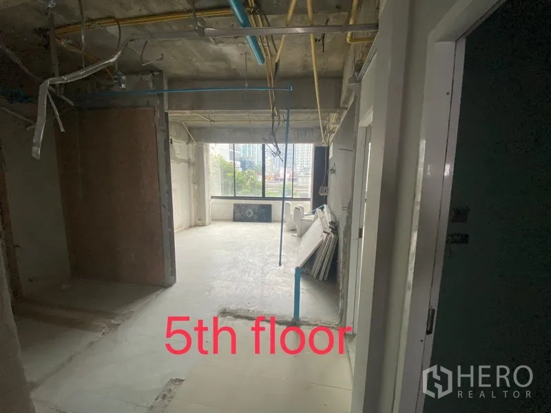 Shophouse for rent in Bang Rak, Bangkok - Fifth-floor room with city view through a large window and unfinished ceiling