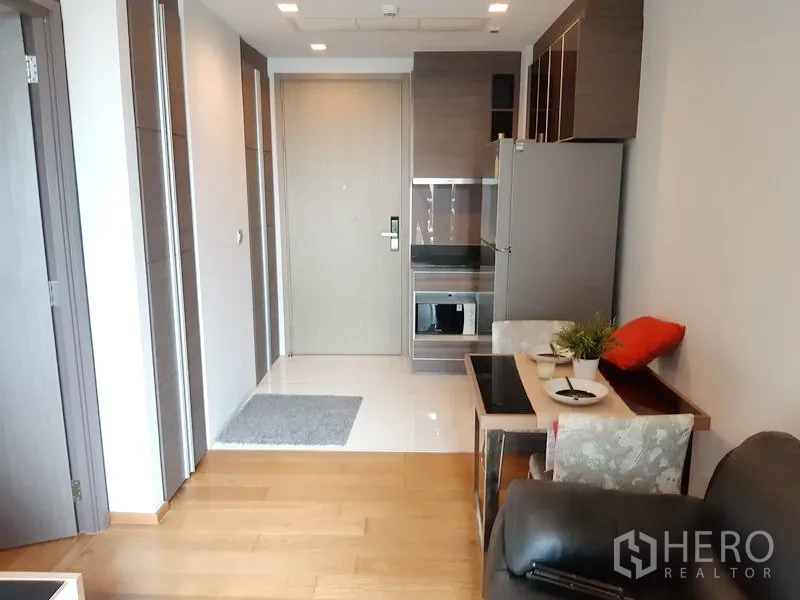 Condominium for rent in Khlong Toei, Bangkok - Compact kitchenette with built-ins, fridge and a small dining nook beside the entry