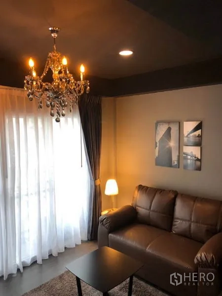 Townhouse for rent in Bang Kapi, Bangkok - Cozy lounge with chandelier, brown sofa, sheer curtains and wall art.