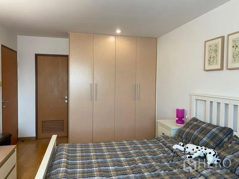 Condominium for sale in Phra Khanong, Bangkok - Bedroom with plaid bedding, large built-in wardrobe, and bedside table.
