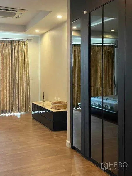 Townhouse for rent in Khlong Toei, Bangkok - Spacious bedroom corner with mirrored wardrobe, wood floor, and full-height curtains.