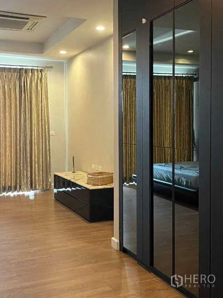 Townhouse for rent in Khlong Toei, Bangkok - Spacious bedroom corner with mirrored wardrobe, wood floor, and full-height curtains.