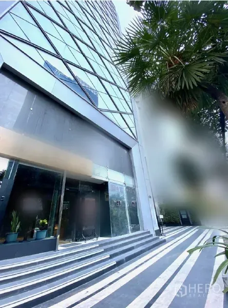 Retail Space for rent in Watthana, Bangkok - Angled exterior view of high-rise retail podium with striped walkway and palm trees.