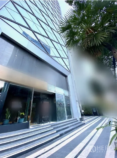 Retail Space for rent in Watthana, Bangkok - Angled exterior view of high-rise retail podium with striped walkway and palm trees.