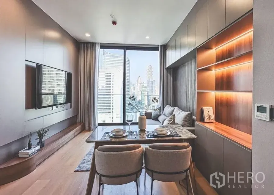 Condominium for rent in Bang Rak, Bangkok - Open-plan living area with dining set and balcony-height glazing framing city views.