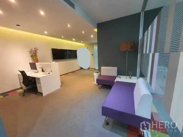 Office Space for rent in Ratchathewi, Bangkok - Modern office reception with purple lounge seating, a work desk, TV wall, and glass partition lighting.