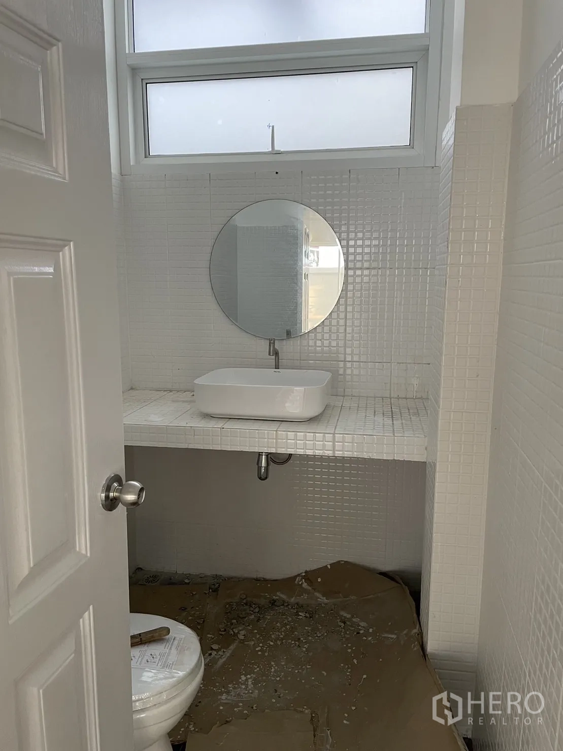 Detached House for rent or sale in Din Daeng, Bangkok - White tiled bathroom with window, round mirror and counter-mounted sink.