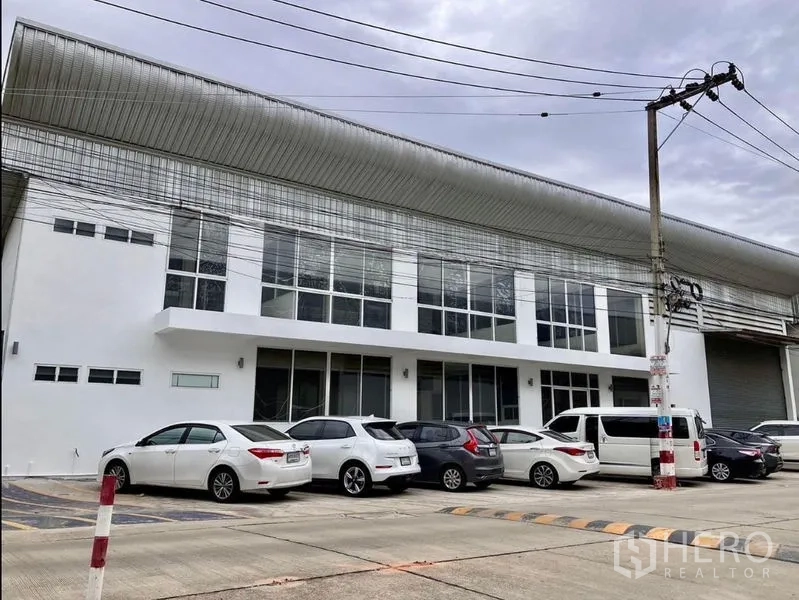 Warehouse for rent in Prawet, Bangkok - Modern white warehouse exterior with glass frontage, parking, and roller shutter access.
