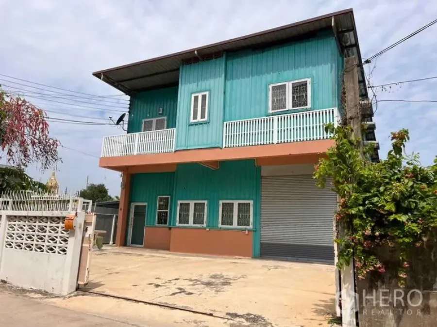 Warehouse for rent in Bang Phli, Samut Prakan - Two-storey turquoise warehouse facade with roller shutter door and balcony.