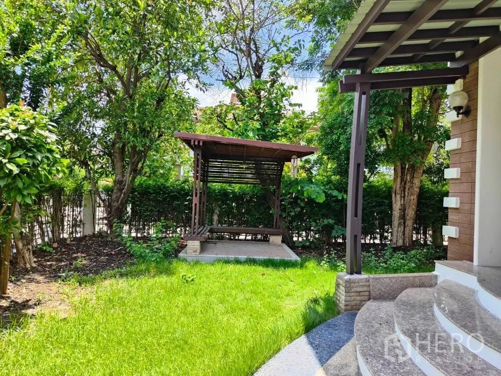 Detached House for rent or sale in Mueang Nonthaburi, Nonthaburi - Green front lawn with a wooden pavilion surrounded by mature trees and hedges.