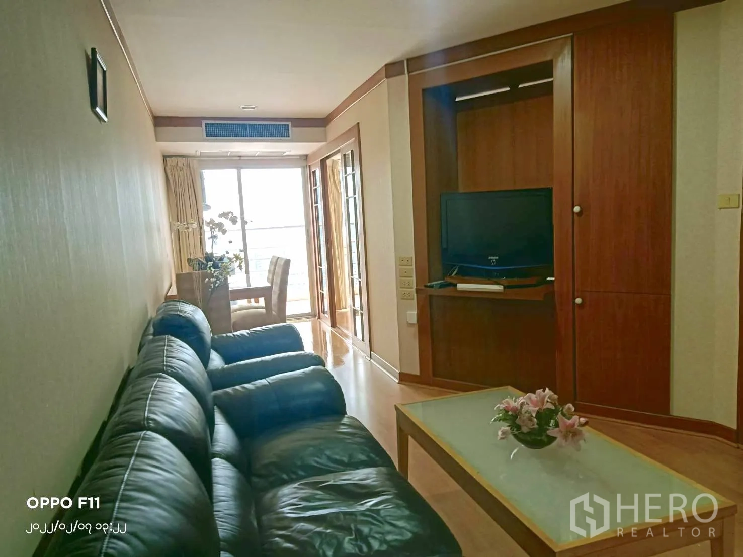 Condominium for rent in Khlong Toei, Bangkok - Long living space with black leather sofa, TV unit and a dining spot by a bright window.