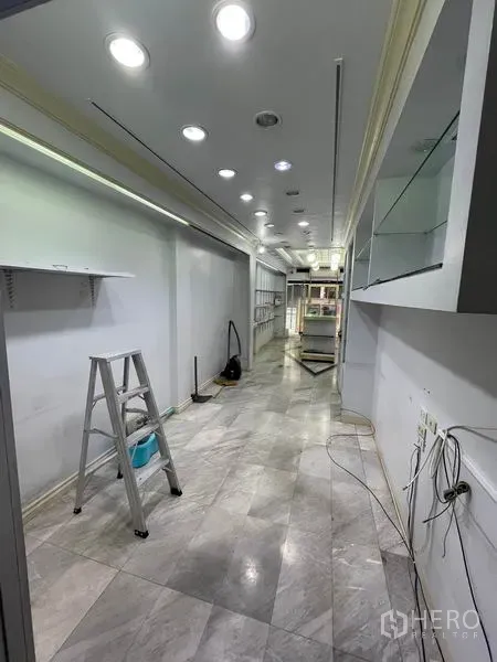 Shophouse for rent in Bang Rak, Bangkok - Long retail interior with recessed ceiling lights, marble floor and shelving in progress.