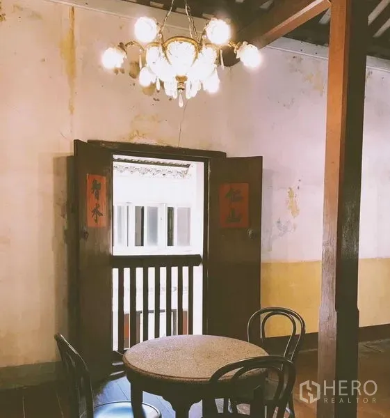 Shophouse for rent in Bang Rak, Bangkok - Small round table under chandelier by wooden balcony doors with Chinese script, vintage décor.