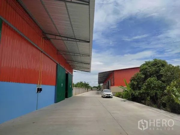 Warehouse for rent in Bang Yai, Nonthaburi - Row of warehouse bays with canopy roofs along a long access road bordered by greenery.
