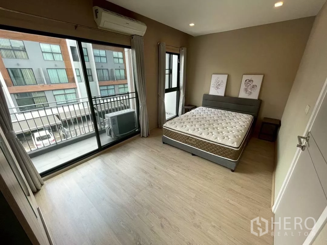 Townhouse for rent in Suan Luang, Bangkok - Spacious bedroom with sliding glass doors opening to a balcony and neighborhood view.