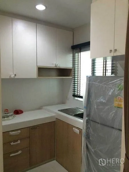 Townhouse for sale in Suan Luang, Bangkok - Compact L-shaped kitchen with cabinets, sink, window blinds and refrigerator.