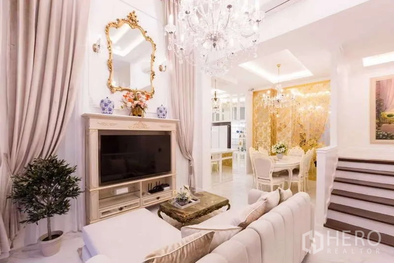 Townhouse for rent in Lat Phrao, Bangkok - Living and dining area with ornate TV console, chandelier and staircase.