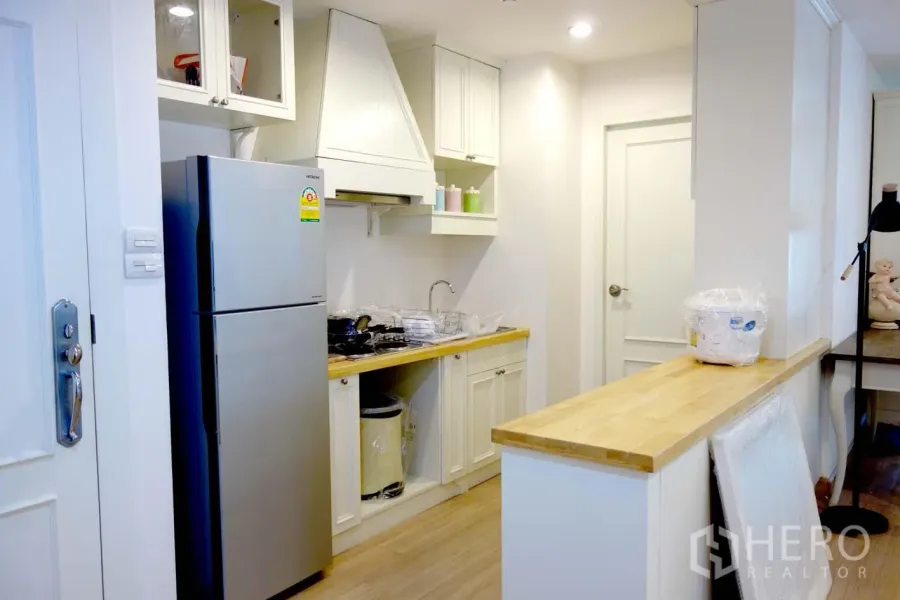 Condominium for rent or sale in Watthana, Bangkok - Bright condo kitchen in Watthana, Bangkok with white cabinetry, wood countertops, stainless refrigerator and gas hob plus a breakfast counter.