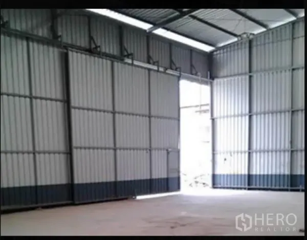 Warehouse for rent in Sai Mai, Bangkok - Spacious warehouse interior featuring a high ceiling, steel cladding, and wide sliding doors allowing natural light.