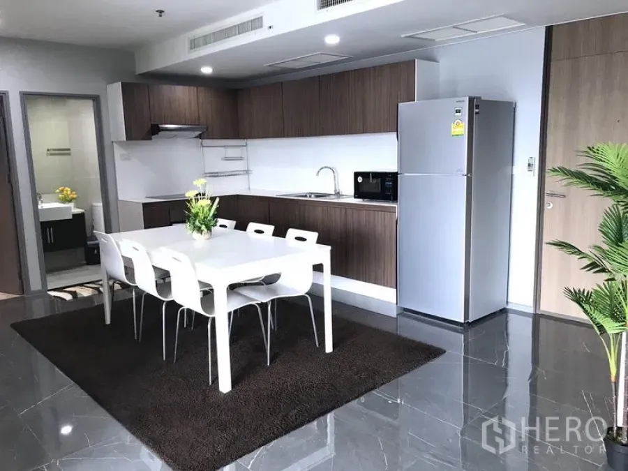 Condominium for rent in Khlong Toei, Bangkok - Kitchen with wood cabinetry, white dining table and stainless-steel refrigerator.