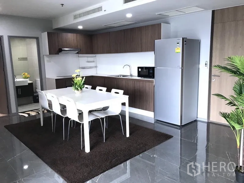 Condominium for rent in Khlong Toei, Bangkok - Kitchen with wood cabinetry, white dining table and stainless-steel refrigerator.